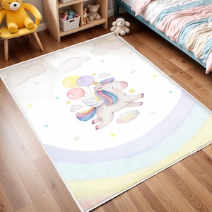 Può includere: Un tappeto bianco con un design a arcobaleno e un unicorno che tiene dei palloncini. L'unicorno è bianco con una criniera e una coda rosa. I palloncini sono rosa, gialli e blu.