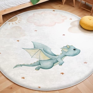 Könnte beinhalten: Ein runder, weißer Teppich mit einem blauen Drachenmuster. Der Drache hat einen hellblauen Körper und gelbe Flügel. Der Teppich hat einen weißen Hintergrund mit braunen Sternen und rosa Wolken.