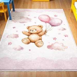 May include: A rectangular children's rug featuring a watercolor design. A brown teddy bear holds pink balloons, surrounded by pink clouds and stars on a white background. The rug has a pink border, suitable for a nursery or playroom.