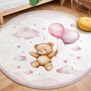 Könnte beinhalten: Ein runder rosa-weißer Teppich mit einem braunen Teddybär, der rosa und lila Ballons hält. Der Teppich hat ein Aquarelldesign mit Wolken und Sternen.