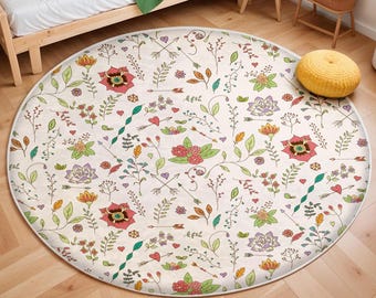 May include: A round, cream-colored rug with a floral pattern. The rug features a variety of flowers, leaves, and arrows in shades of pink, red, green, and yellow.