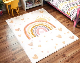 May include: A white rug with a pink, yellow, and purple rainbow design. The rainbow has a sun above it and is surrounded by small pink hearts.
