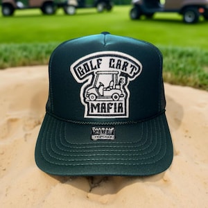 May include: A dark green trucker hat with a white embroidered patch that says "Golf Cart Mafia" and a cartoon golf cart. The hat has a black mesh back.
