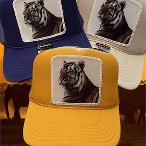 May include: Three trucker hats with a tiger patch on the front. The hats are in blue, beige, and yellow. The tiger patch is a close-up of a tiger's face.