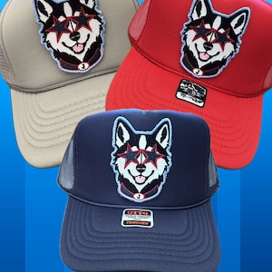 May include: Three trucker hats with a black and white husky dog wearing sunglasses and a red, white, and blue collar. The hats are gray, red, and navy blue.