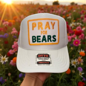 May include: White trucker hat with a white foam front and mesh back. The hat features the text "PRAY FOR BEARS" in gold and green lettering. The hat has a durable snap closure and is labeled "OTTO" on the front.