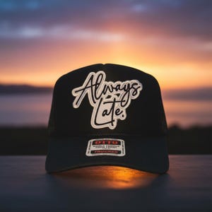 May include: Black trucker hat with the text "Always Late" in white script. The hat has a mesh back and a curved brim. The Otto brand label is visible on the front.