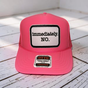 May include: A bright pink trucker hat with a white patch featuring the words "immediately. NO." in black. The hat has a mesh back and a curved brim. The hat also has a small tag that says "OTTO" and "TRUCKER".