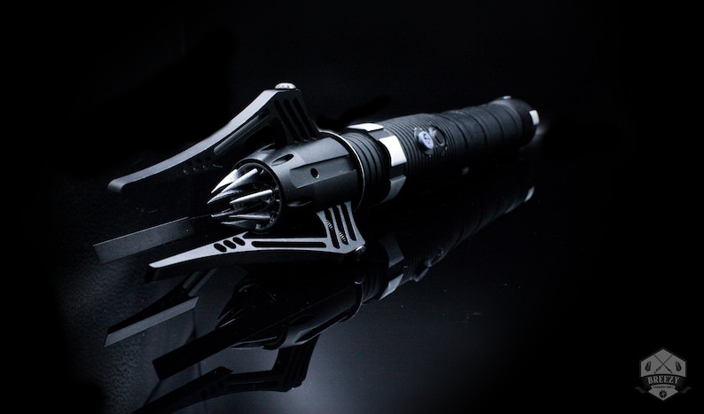 May include: A black metal weapon with a spiked head and a textured handle. The weapon is lying on a black surface.