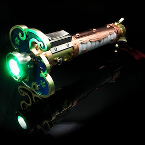 May include: A green lightsaber with a copper and white handle. The handle is decorated with intricate details and a gold-colored accent. The lightsaber is lit and glowing green.