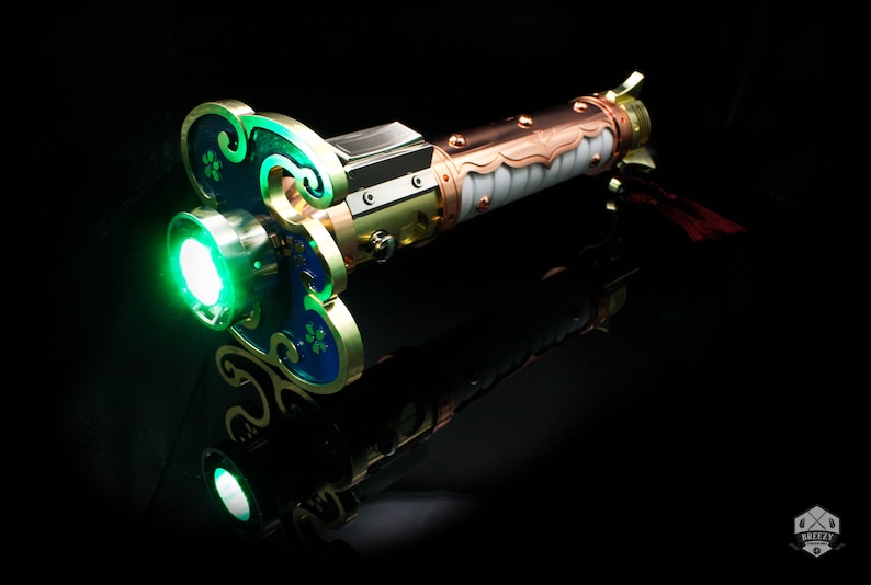 May include: A green lightsaber with a copper and white handle. The handle is decorated with intricate details and a gold-colored accent. The lightsaber is lit and glowing green.