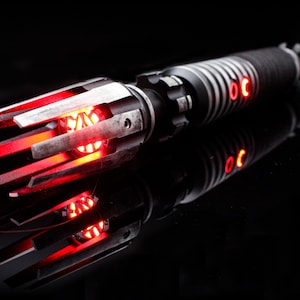 May include: A red lightsaber with a black and silver handle and a detailed, intricate emitter. The lightsaber is lit and glowing red.