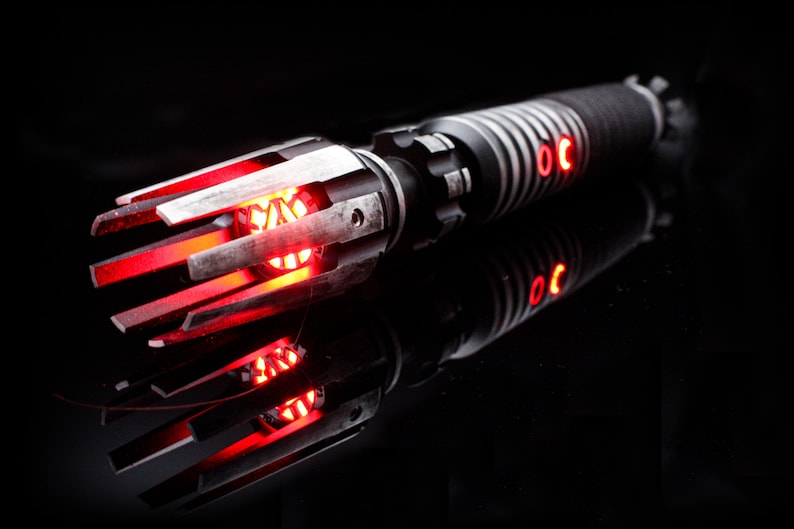 May include: A red lightsaber with a black and silver handle and a detailed, intricate emitter. The lightsaber is lit and glowing red.