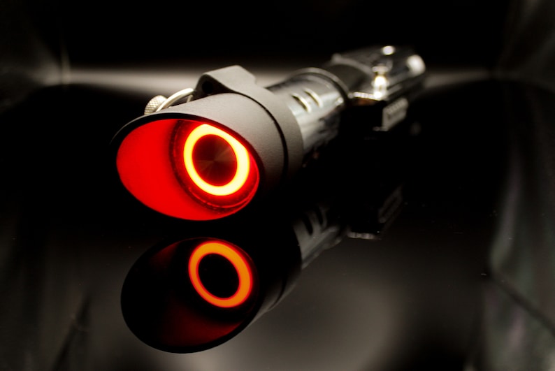 May include: A black lightsaber with a red glowing blade. The lightsaber is on a black surface.