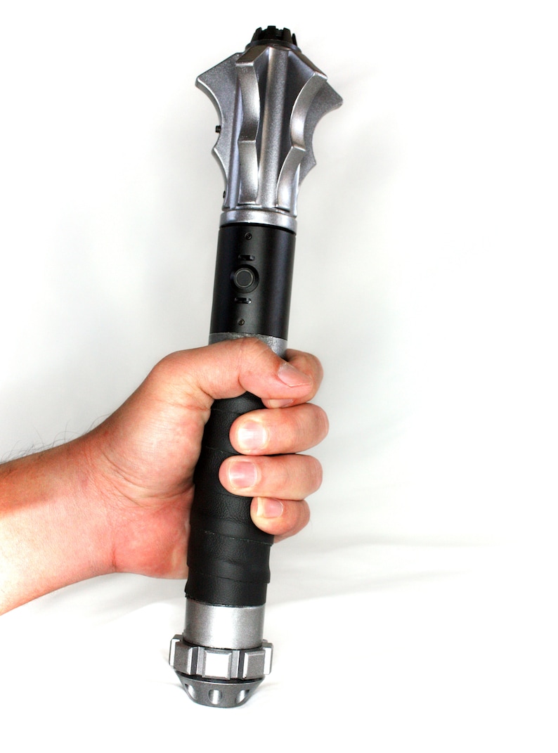 May include: A silver and black handheld weapon with a spiked head and a textured black grip.