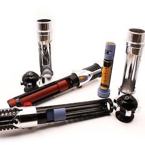 May include: A disassembled lightsaber with a black and silver handle, a red and brown middle section, and a silver and blue tip. The lightsaber is in pieces, with the handle, middle section, and tip separated. There are also two silver lightsaber hilt extensions.