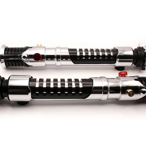 May include: Two black and silver lightsaber hilts with red buttons. The hilts have a textured grip and a black and silver design.
