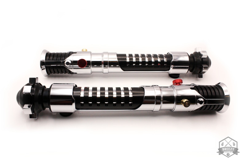 May include: Two black and silver lightsaber hilts with red buttons. The hilts have a textured grip and a black and silver design.