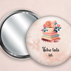 May include: A compact mirror with a white background featuring a stack of books, a teacup, and pink flowers. The text "Votre texte ici" is printed below the image.