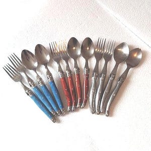May include: A selection of stainless steel cutlery, including forks and spoons. The handles are in three colours: blue, red, and silver. The utensils are arranged in a fan shape, ideal for a dinner setting.