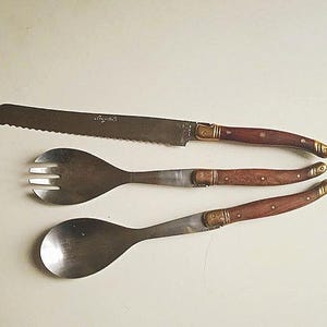 May include: A set of three silver utensils with wooden handles. The set includes a knife, a fork, and a spoon.