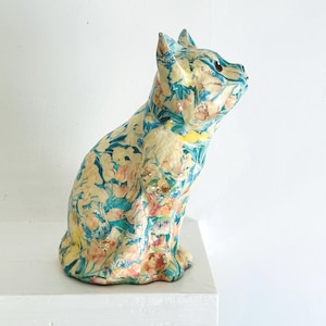 May include: A ceramic cat figurine with a floral pattern in shades of blue, pink, and yellow. The cat is sitting with its head turned to the side.