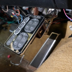 Może przedstawiać: Chromowany panel sterowania z czarną powierzchnią i wieloma przyciskami. Panel jest oznaczony jako "e-LEVEL" i "e-ADJUST".