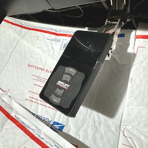 May include: A black air suspension control unit with a red and white logo that says "AirLift Performance". The unit has several buttons and a display screen.