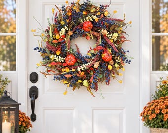 May include: A circular autumn wreath featuring small orange pumpkins, clusters of dark blue berries, cream-colored berries, and various dried leaves in shades of yellow, red, and brown, arranged on a circular frame for display on a door.
