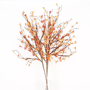 May include: A decorative artificial branch with numerous thin, dark brown stems and small, colorful leaves. The leaves transition in color from red to orange and yellow, creating a vibrant autumn aesthetic. The branch is displayed in a clear glass vase against a white background.