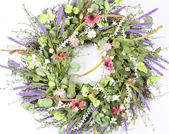 May include: A spring-themed wreath with lavender, pink, and white flowers, and green leaves. The wreath is made of twigs and has a natural, rustic look.