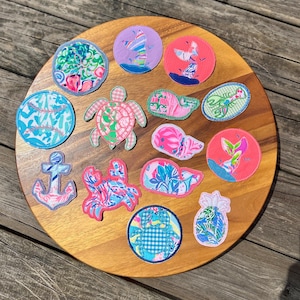 May include: A collection of fourteen fabric patches featuring various shapes including a sea turtle, crab, anchor, pineapple, baseball, and mermaid tails. The patches display vibrant, multi-colored floral and geometric patterns with stitched edges.