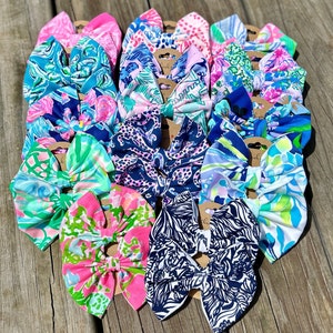 May include: A collection of colorful hair bows with various patterns, including floral, geometric, and animal prints. The bows are made of fabric and have a blue, pink, and green color scheme.