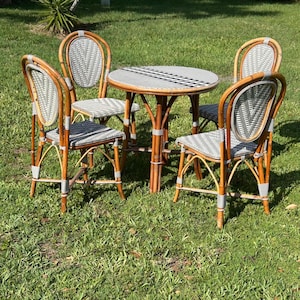 May include: A bistro set consisting of a round table and four chairs, all constructed from brown rattan-style frames with woven seats and backrests featuring a white and grey geometric chevron pattern. The furniture has a light brown finish.