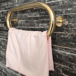 以下が含まれることがあります： 黒いスレートタイルの壁に取り付けられた金色のタオルバー。ピンクのタオルがバーにかけられています。