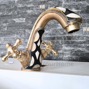 Op de afbeelding: Een gouden badkamerkraan met een zwart-wit patroon. De kraan heeft twee kruisvormige handvatten.