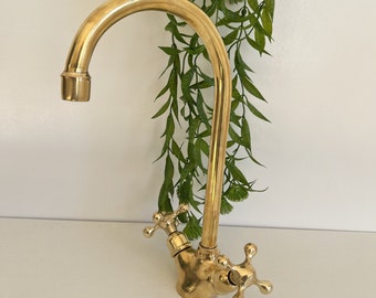 May include: A gold-toned kitchen faucet with a high-arc spout and cross-shaped handles.