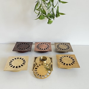 Könnte beinhalten: Fünf verschiedene Abflussabdeckungen in verschiedenen Ausführungen, darunter Messing, Kupfer und Bronze. Die Abflussabdeckungen sind rund und haben ein dekoratives Design.