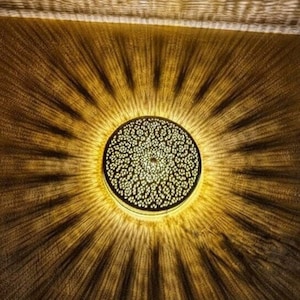 May include: A round, gold-colored ceiling light fixture with a decorative, intricate pattern. The light casts a warm, golden glow on the surrounding surface.