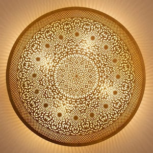 Może przedstawiać: Okrągła, złota lampa sufitowa z misternym, geometrycznym wzorem. Światło jest włączone i oświetla wzór.