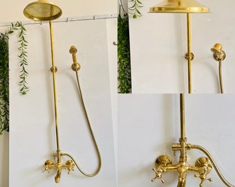 May include: A gold-colored shower fixture with a round showerhead and a handheld showerhead. The fixture includes a faucet with cross-shaped handles and a long, vertical pipe. The showerhead is round and has small holes.