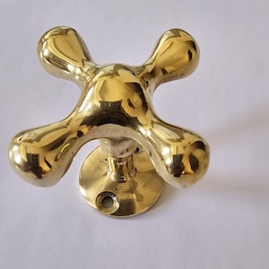 May include: A gold-toned brass door knob with a cross-shaped design. The knob has four rounded protrusions and a circular base.