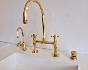 May include: A gold-toned kitchen faucet with two handles and a separate spout. The faucet is mounted on a white countertop.