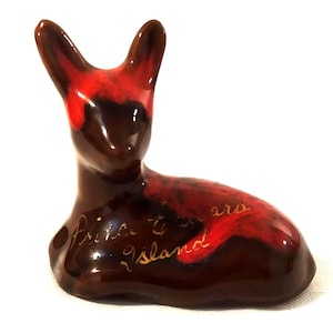 Puede incluir: Una figurita de cerámica roja y marrón de un ciervo con letras doradas que dicen "Prince Edward Island".