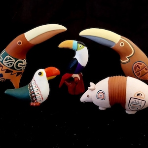 May include: Five hand-painted ceramic figurines of toucans and an armadillo. The toucans are in various colors, including brown, yellow, blue, and green. The armadillo is brown and white with geometric patterns.