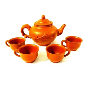 Peut inclure: Un service à thé en terre cuite composé d'une théière et de quatre tasses. La théière est ornée d'un motif floral et d'un couvercle. Les tasses sont simples et rondes.