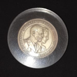 Puede incluir: Una moneda de plata con una imagen de perfil de un hombre y una mujer. La moneda dice "His Excellency The Governor General And Lady Alexander".