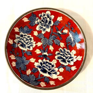 May include: A red and white porcelain bowl with a blue floral design. The bowl has a brass rim.