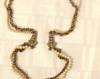 Puede incluir: Un collar de cadena dorada con una hebra de perlas, con dos acentos decorativos de oro y cristal.