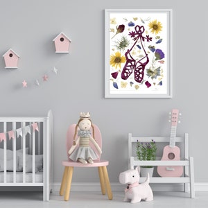 Puede incluir: Una impresi&oacute;n enmarcada de un par de zapatillas de ballet rojas hechas de flores y hojas prensadas. La impresi&oacute;n est&aacute; colgada en una pared gris claro en una guarder&iacute;a con una cuna, una silla rosa y una guitarra de juguete.